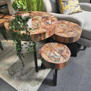 May include: Three round wooden tables with a geometric pattern of colourful wood pieces. The tables are nested together and have black metal legs.