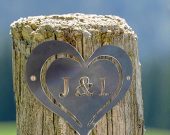 May include: A metal heart-shaped sign with the initials "J & L" cut out, attached to a weathered wooden post.