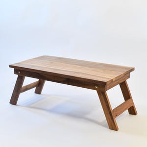 May include: A wooden folding table with a natural brown finish. The table has a rectangular top and two sets of legs that fold out.