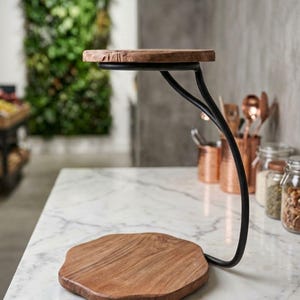 May include: A two-tiered display stand featuring a black metal frame with a curved support arm and two circular, natural-edged wooden platforms. The top platform is smaller than the base, creating a tiered structure for displaying items.