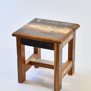 May include: A small wooden stool with a multi-coloured top made from reclaimed wood. The stool has a simple design with four legs and a single crossbar.