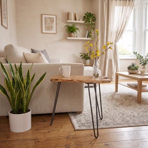 May include: A small side table with a natural wood slab top and three thin black metal hairpin legs. A white ceramic mug sits on the table surface next to a clear glass vase containing yellow flowering branches. The table is placed on a wooden floor.