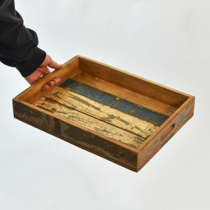 May include: Rectangular wooden serving tray with a distressed finish. The tray features a natural wood color with blue and white painted accents. It has built-in handles for easy carrying.