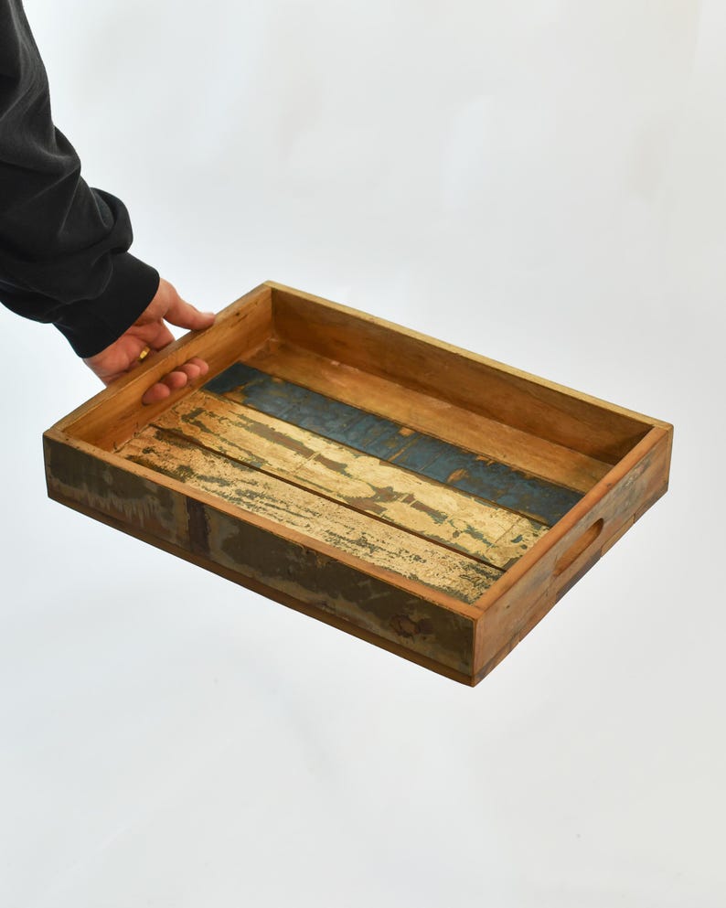 May include: Rectangular wooden serving tray with a distressed finish. The tray features a natural wood color with blue and white painted accents. It has built-in handles for easy carrying.