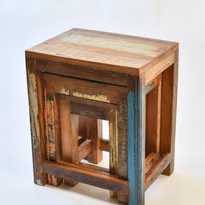 May include: A set of two nesting tables made from reclaimed wood. The tables have a rustic, distressed look with a mix of brown, blue, and green paint. The top table is larger than the bottom table and they can be used together or separately.