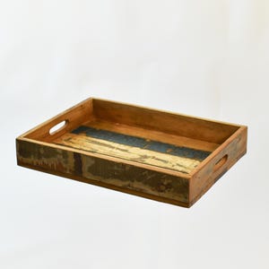 May include: Rectangular wooden serving tray with cut-out handles. The tray features a distressed finish with shades of brown, blue, and gold. The tray is empty and sits on a white background.