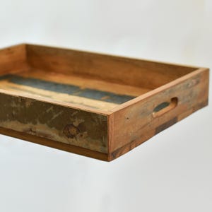 May include: A rectangular wooden serving tray with a distressed finish. The tray has a natural wood color with a dark blue and green accent in the center. It features built-in handles for easy carrying.