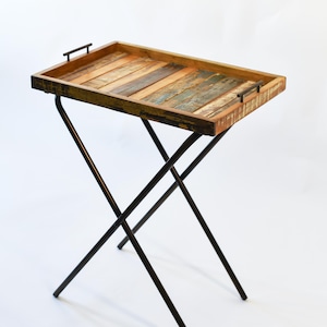 May include: A wooden tray table with a rustic, reclaimed wood top and black metal legs. The tray has a handle on each side.