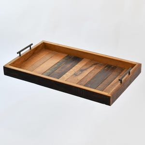 May include: A rectangular wooden tray with a dark brown wood frame and a light brown wood interior. The tray has two metal handles on the sides.