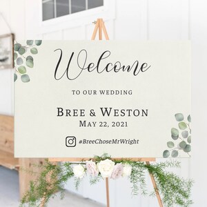 May include: Welcome sign with greenery and calligraphy. The sign reads "Welcome to our wedding, Bree & Weston, May 22, 2021, #BreeChooseMrWright".