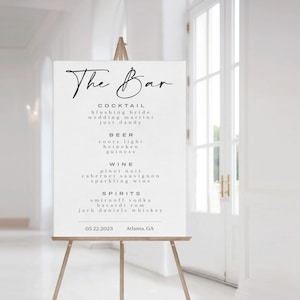 May include: A white sign with black text listing the bar menu for a wedding reception. The sign reads "The Bar" at the top and lists cocktails, beer, wine, and spirits. The date and location are listed at the bottom: 05.22.2023 Atlanta, GA.