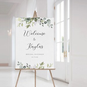 May include: A white welcome sign with green watercolor floral accents. The sign reads "Welcome to Kayla's Bridal Shower 4.17.23".