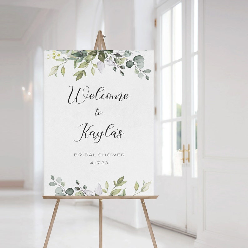 May include: A white welcome sign with green watercolor floral accents. The sign reads "Welcome to Kayla's Bridal Shower 4.17.23".