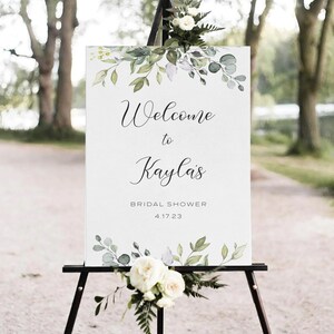 May include: White sign with green watercolor leaves and the text "Welcome to Kayla's Bridal Shower 4.17.23" on an easel.