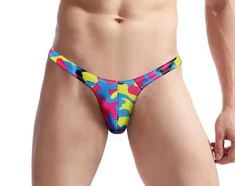 May include: A colorful, patterned thong with a low rise and a thin strap. The pattern is a camouflage design with pink, blue, yellow, and black colors.