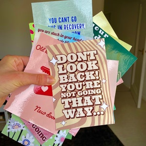 May include: A stack of colorful cards with motivational quotes. The top card is pink with brown text that reads "Don't look back! You're not going that way..."