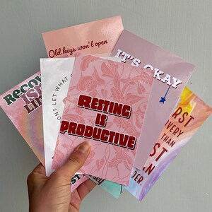 May include: Five pink and white cards with inspirational quotes. The quotes are "Old keys won't open", "Resting is Productive", "It's Okay", "Don't Let What Limits You", and "First is Very Than Second".