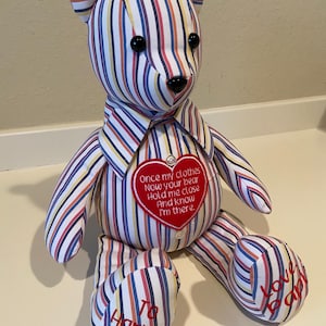 May include: A handmade teddy bear with a striped pattern in red, blue, yellow, and white. The bear has black button eyes and a black nose. A red heart-shaped patch on the chest has embroidered text. The bear's foot reads "To Harper" and "Love baby".