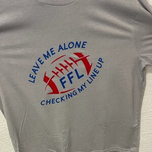 Puede incluir: Camiseta gris con un gráfico rojo y azul de un balón de fútbol con el texto "LEAVE ME ALONE CHECKING MY LINEUP FFL"