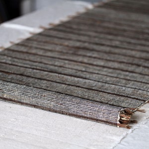 Pode incluir: Um corredor de mesa tecido marrom e branco com uma borda franjada. O corredor est&aacute; enrolado e sobre uma toalha de mesa de linho branco.