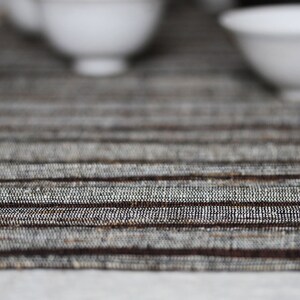 Pode incluir: Um close-up de um  placemat tecido em listras marrons e brancas. O placemat tem um brilho sutil e uma superf&iacute;cie texturizada.