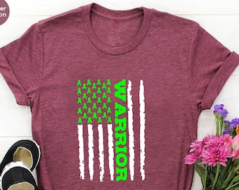 May include: Heather maroon t-shirt with a green ribbon American flag design and the word "WARRIOR" printed vertically on the right side of the flag.