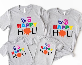May include: A set of four grey t-shirts with the text "Happy Holi" in colorful letters and handprints. The shirts are in different sizes for adults and children.