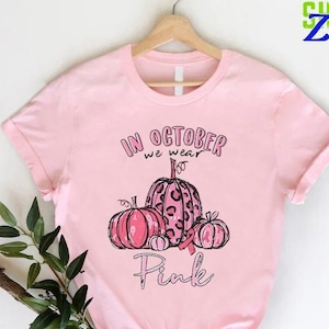 May include: Pink t-shirt with a graphic of pink pumpkins with a pink ribbon and the text "In October we wear Pink".