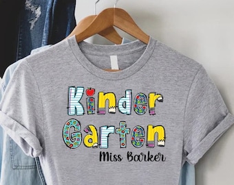 May include: Gray t-shirt with the text "Kinder Garten" in colorful letters and "Miss Barker" below.