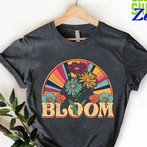 May include: A dark gray t-shirt with a retro-style graphic of a rainbow and flowers with the word "BLOOM" in yellow letters.
