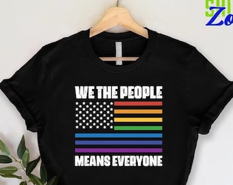 Puede incluir: Camiseta negra con una bandera americana arcoíris y el texto "We the People Means Everyone".