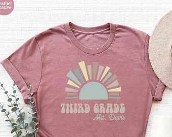 May include: A heather mauve t-shirt featuring a retro-style sun graphic and the text "Third Grade" with the teacher's name "Mrs. Davis" underneath.