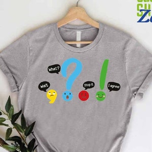 May include: Gray t-shirt with a graphic of punctuation marks with faces and speech bubbles. The text on the shirt reads "Wait", "What?", "Stop it", and "I agree!"