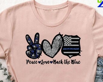 May include: A pink t-shirt with a peace sign, heart, and a police badge with a thin blue line. The text "Peace Love Back the Blue" is printed below the design.