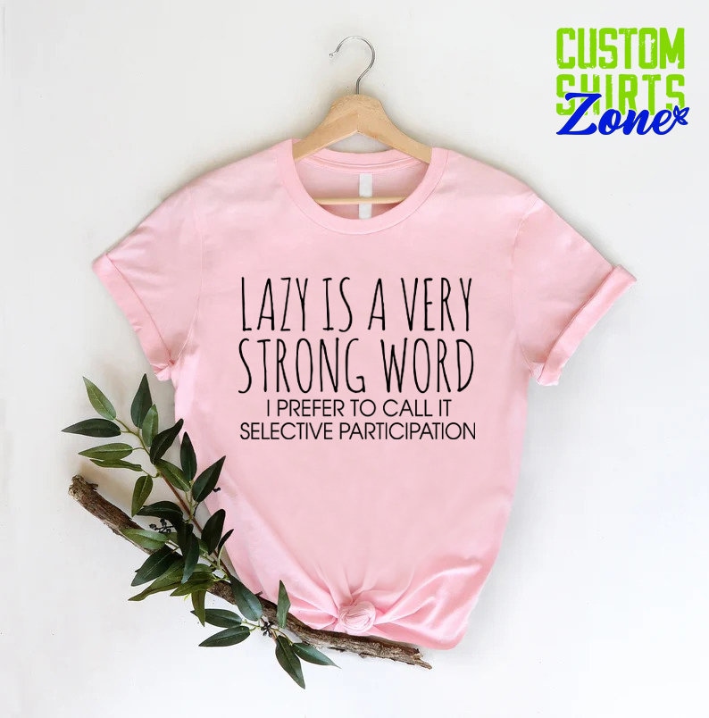 May include: Pink t-shirt with the text "LAZY IS A VERY STRONG WORD I PREFER TO CALL IT SELECTIVE PARTICIPATION" printed in black.