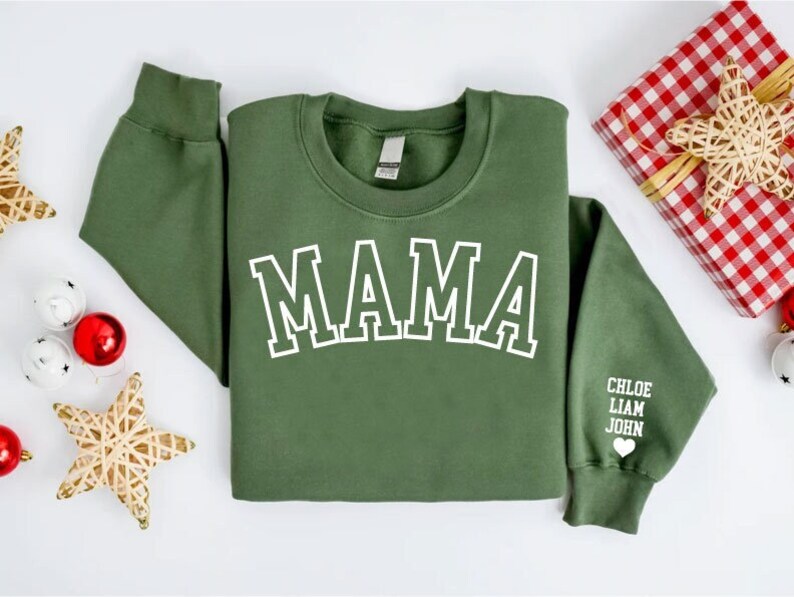 Puede incluir: Sudadera verde con la palabra "MAMA" en letras blancas en la parte delantera. La manga tiene los nombres "CHLOE, LIAM, JOHN" y un peque&ntilde;o coraz&oacute;n impreso en blanco.
