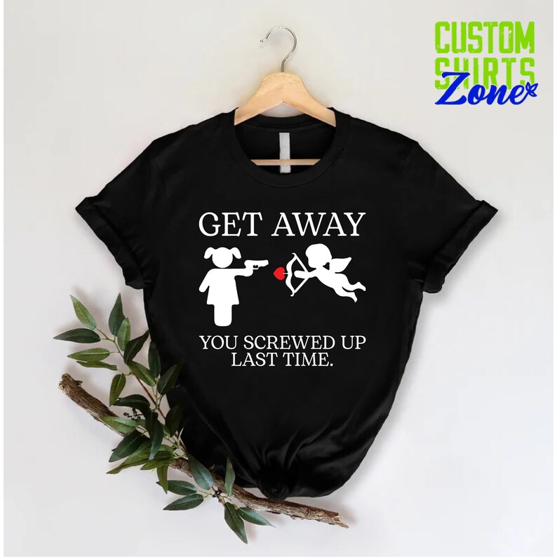 May include: Black t-shirt with a white graphic of a girl holding a gun and a cupid with an arrow. The text on the shirt reads "GET AWAY YOU SCREWED UP LAST TIME."