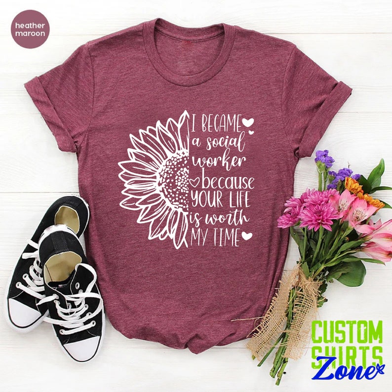 May include: A heather maroon t-shirt with a white sunflower graphic and the text "I became a social worker because your life is worth my time".