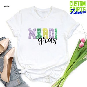 May include: White t-shirt with the text "Mardi Gras" in purple, green, and gold letters with a leopard print pattern.