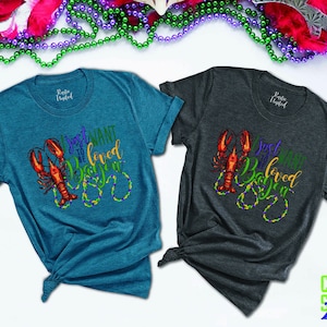 May include: Two teal and gray t-shirts with a crawfish and beads design. The text on the shirts reads "I just want to be loved in Baton Rouge".