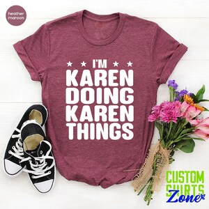 May include: A heather maroon t-shirt with the text "I'm Karen Doing Karen Things" in white. The shirt is laid flat on a white surface with a pair of black sneakers and a bouquet of pink and purple flowers.