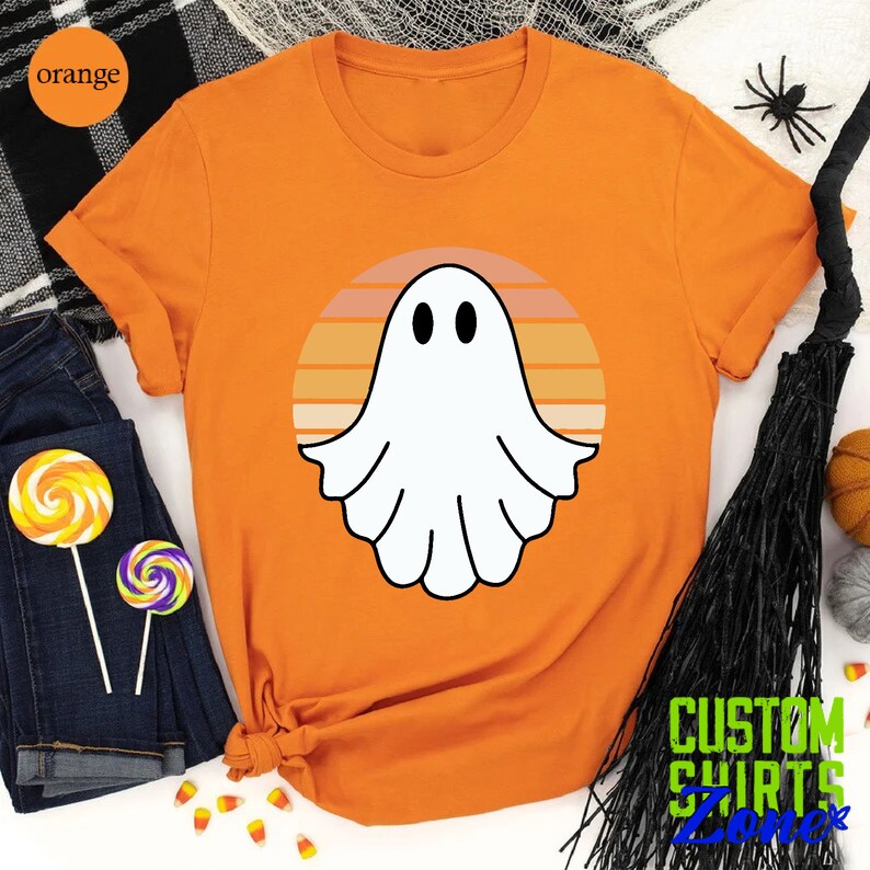 May include: Orange t-shirt with a white ghost graphic in front of a retro sunset design. The text "CUSTOM SHIRTS ZONE" is visible in the bottom right corner of the image.