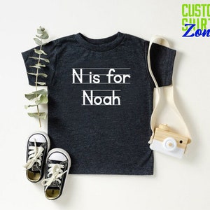 May include: A dark gray t-shirt with white text that says "N is for Noah".
