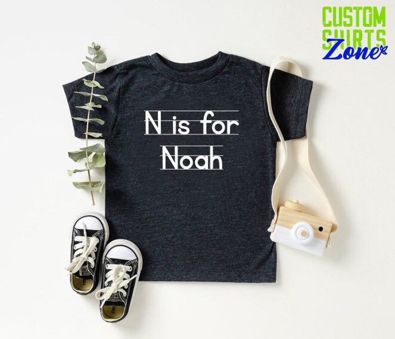 May include: A dark gray t-shirt with white text that says "N is for Noah".