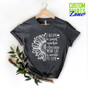 May include: A dark gray t-shirt with a white sunflower graphic and the text "I became a social worker because your life is worth my time".
