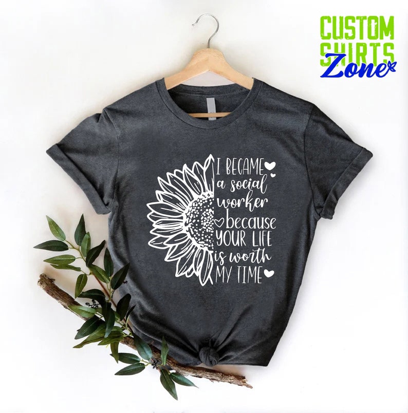 May include: A dark gray t-shirt with a white sunflower graphic and the text "I became a social worker because your life is worth my time".