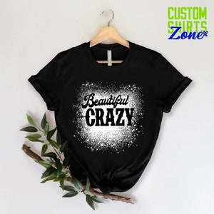 Puede incluir: Camiseta negra con un dise&ntilde;o de salpicaduras blancas y el texto "Beautiful Crazy" en negro.