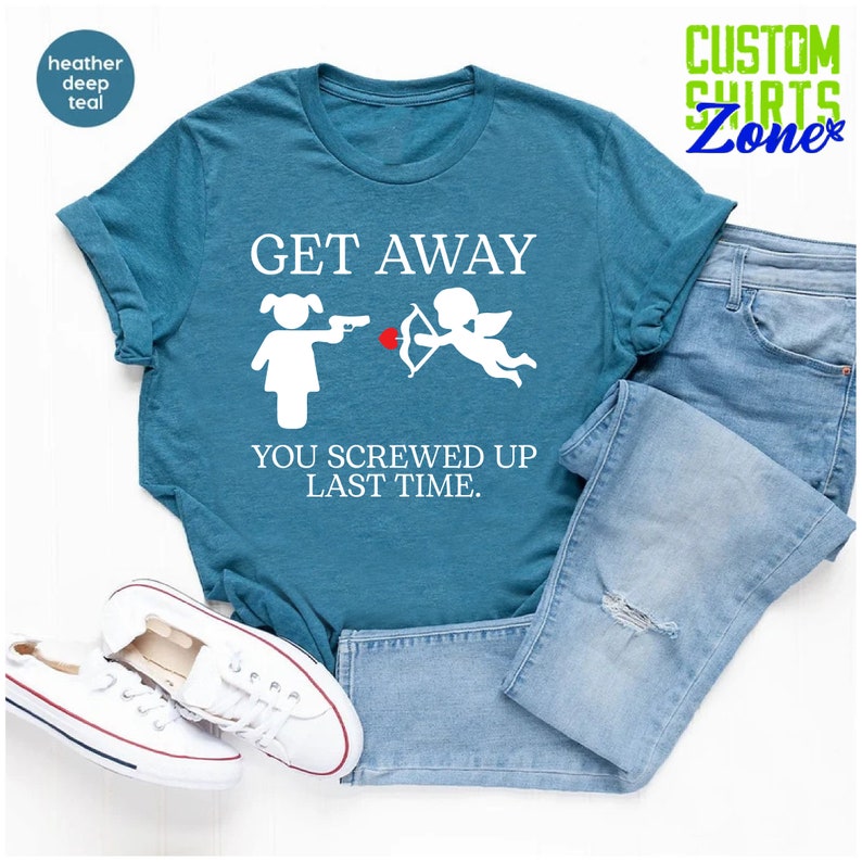 May include: A teal blue t-shirt with the text "GET AWAY YOU SCREWED UP LAST TIME."  The text is in white and there is a white illustration of a woman pointing a gun at a cupid with an arrow.