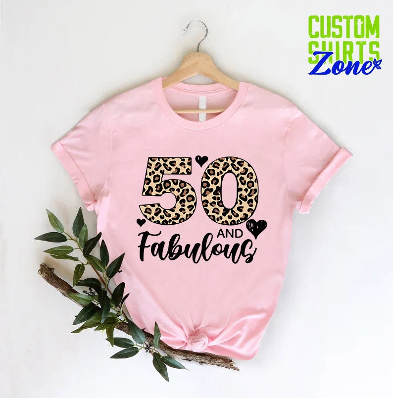 K&ouml;nnte beinhalten: Rosa T-Shirt mit einem Leopardenmuster 50 und dem Text "and Fabulous" in Schwarz.