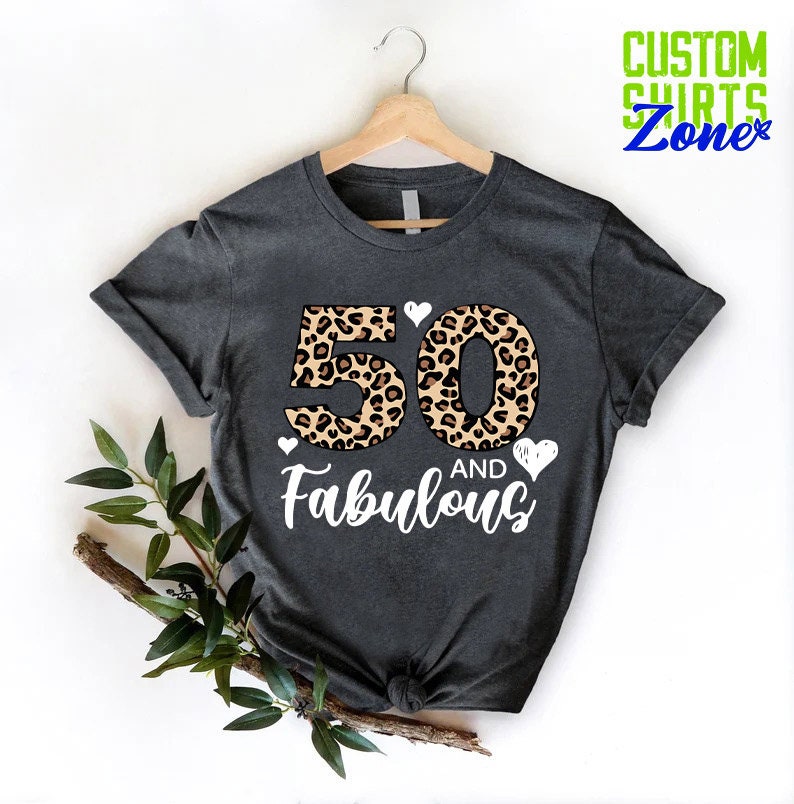 K&ouml;nnte beinhalten: Ein dunkelgraues T-Shirt mit einer Leopardenmuster-Nummer 50 und dem Text "AND Fabulous" in Wei&szlig;.